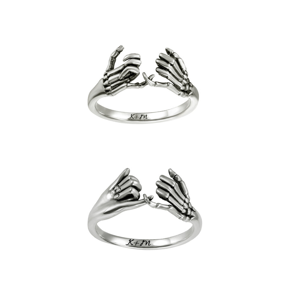 Silver pinky promise ring with engraved initials K+M on the band, showcasing a skeleton hand design.
