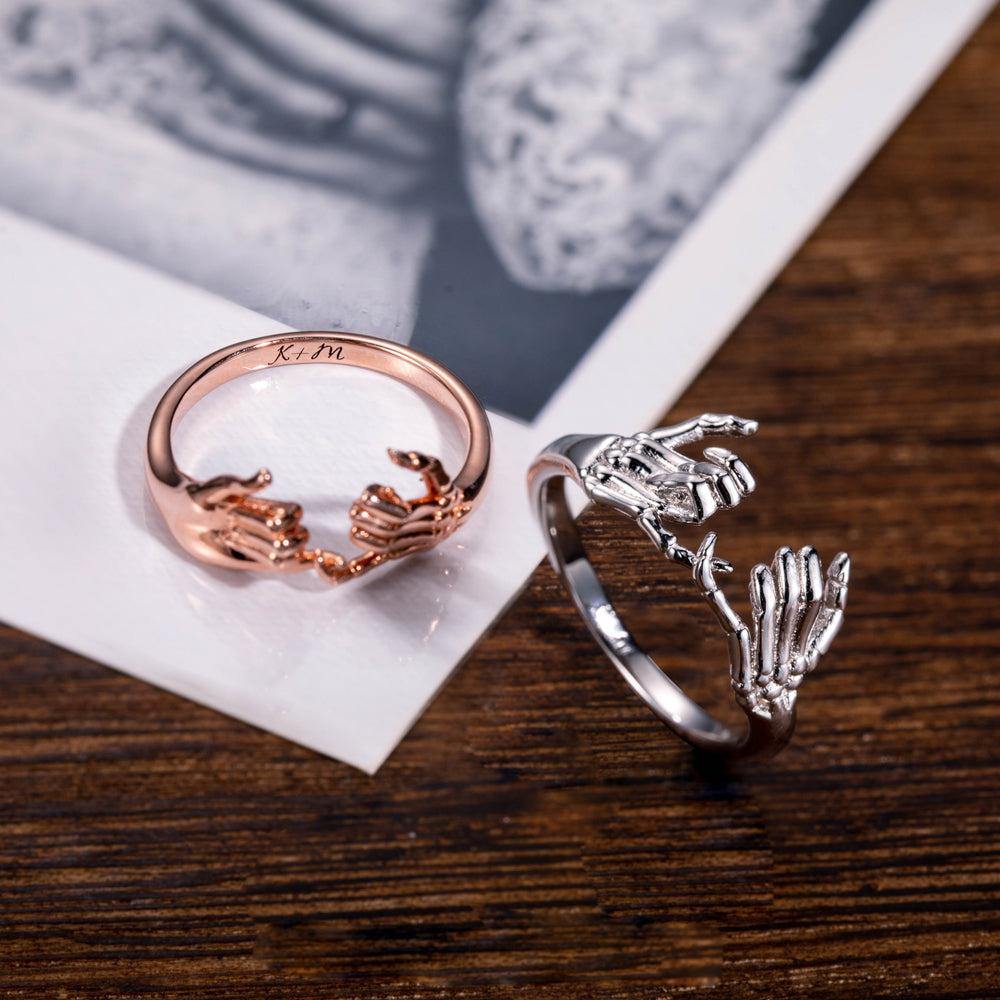 Rose gold and silver pinky promise rings with 'K+M' engraving on wooden surface beside monochrome photos.