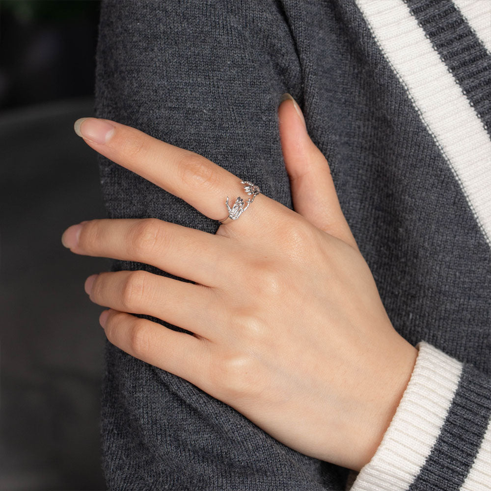 Person wearing a silver pinky promise ring with skeletal hand design on the middle finger, against a grey sweater.