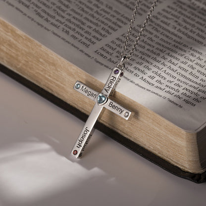 Close-up of a personalized heart cross necklace with names and birthstones on a silver chain, placed on an open Bible, symbolizing faith and love.
