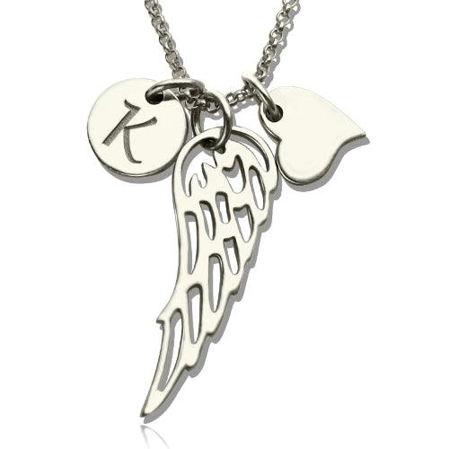A silver necklace with three charms: a circular disc with the letter "K," an angel wing, and a heart, displayed on a white background.