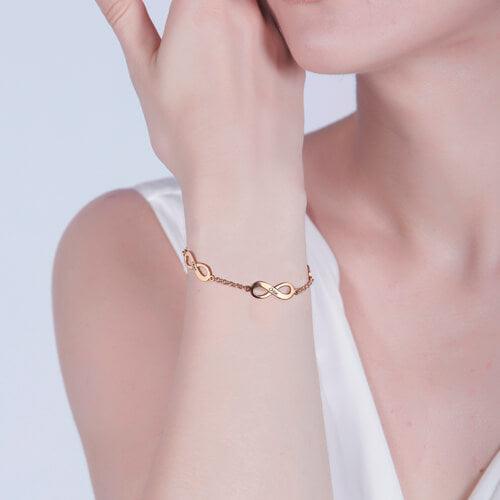 A woman wearing a rose gold infinity bracelet with a chain link design. The bracelet elegantly rests on her wrist as she gently touches her face.