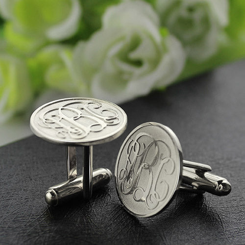 Silver monogram cufflinks with intricate design on black leather, white roses in the background.
