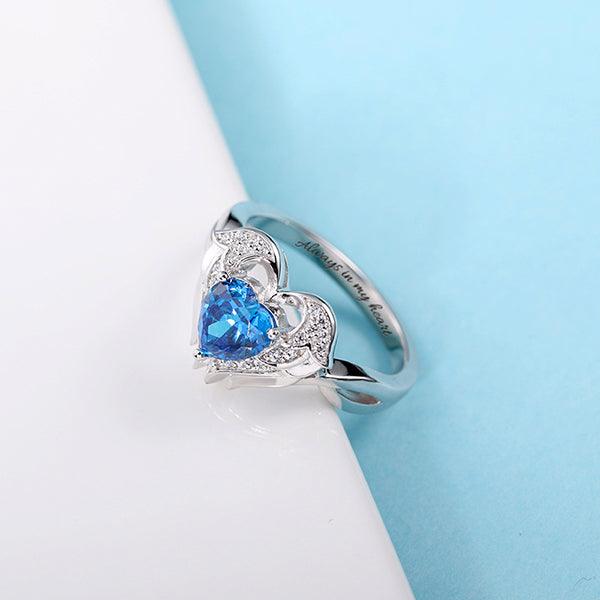 Silver angel wing heart ring with blue stone and 'Always in my heart' engraving, on blue and white CG274-3 - 600 x 600px