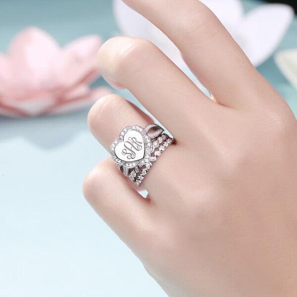  "Hand showing a silver heart-shaped monogram ring with crystal-studded stackable bands."