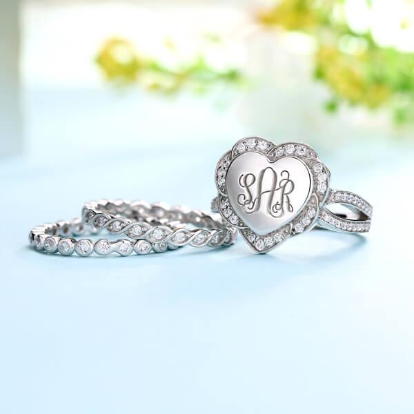 Silver heart-shaped monogram ring with engraved initials, paired with coordinating stackable bands.