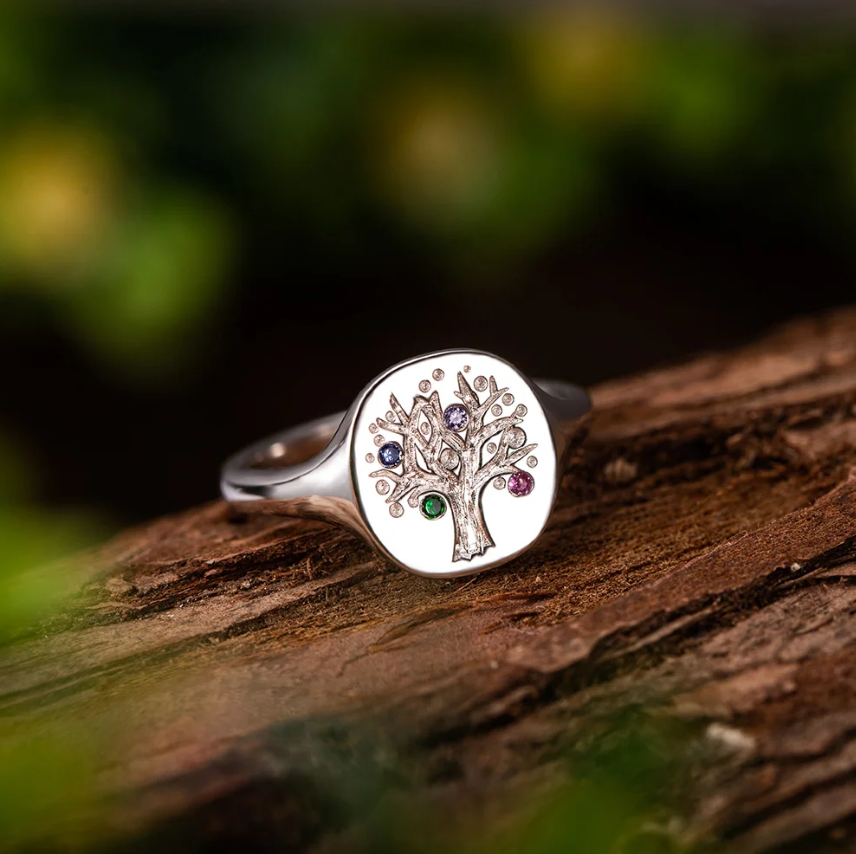 A silver ring with a tree design inset with multi-colored birthstones on a wooden surface.