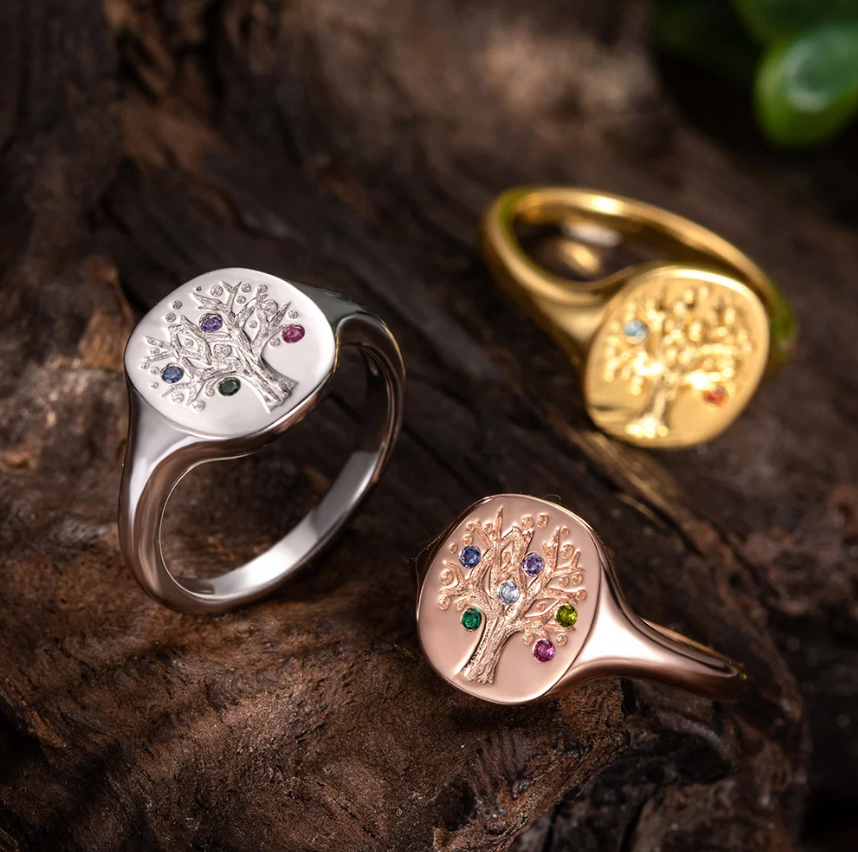 Three family tree rings with birthstones on wood; silver, rose gold, and gold finishes.