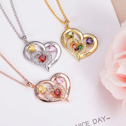 Three heart-shaped pendants with colorful gemstones, engraved with names, in silver, gold, and rose gold, placed on a light background with pink roses.
