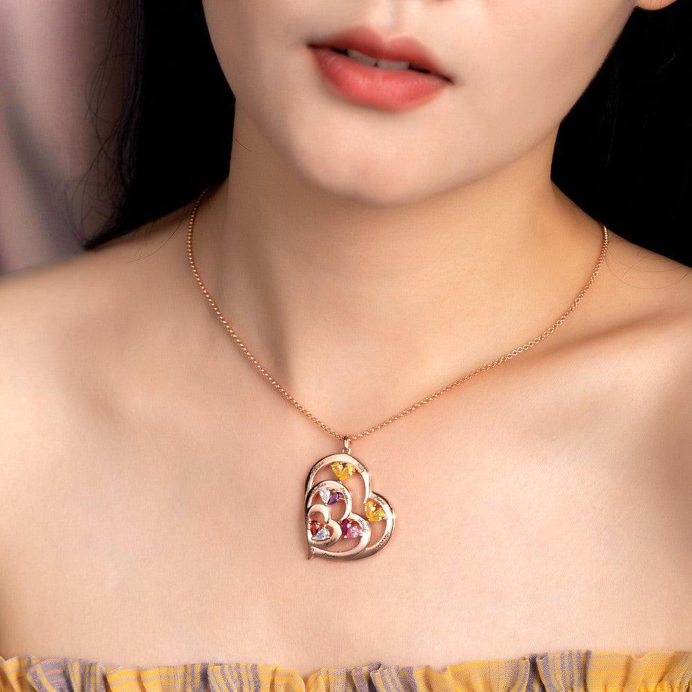 A woman wearing a heart-shaped pendant with colorful gemstones on a delicate chain, highlighting the jewelry against her bare skin and a yellow off-shoulder top.
