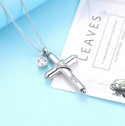 Silver cremation cross necklace with infinity symbol and crystal pendant, on a blue background with a 'LEAVES' booklet.