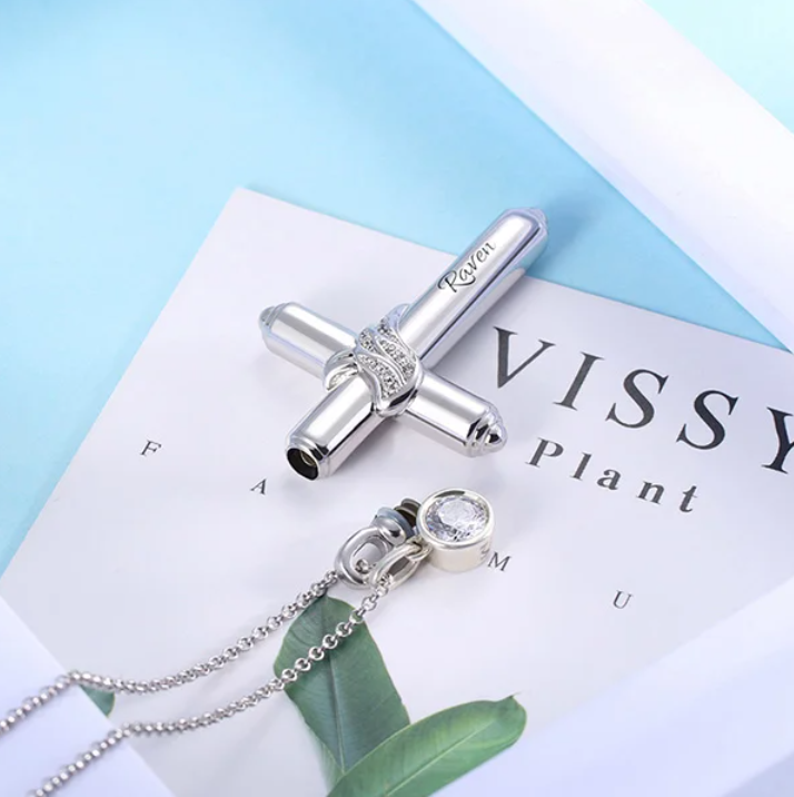 Silver cremation cross necklace with an infinity symbol wrap and crystal pendant on a 'VISSY Plant' booklet.