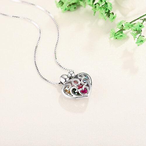 Silver heart-shaped pendant with decorative swirls and colorful gems on a necklace, set against a soft background.