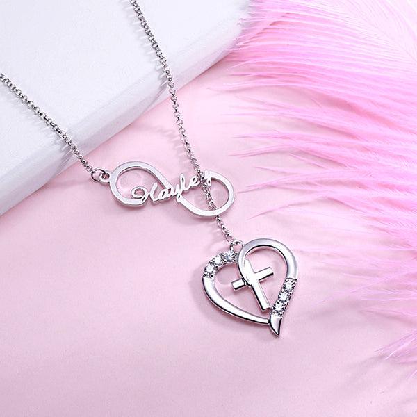 Silver Infinity Heart Name Necklace with Custom Birthstone, featuring a heart and cross design, personalized with the name "Hayley" and sparkling birthstones, displayed on a pink background.