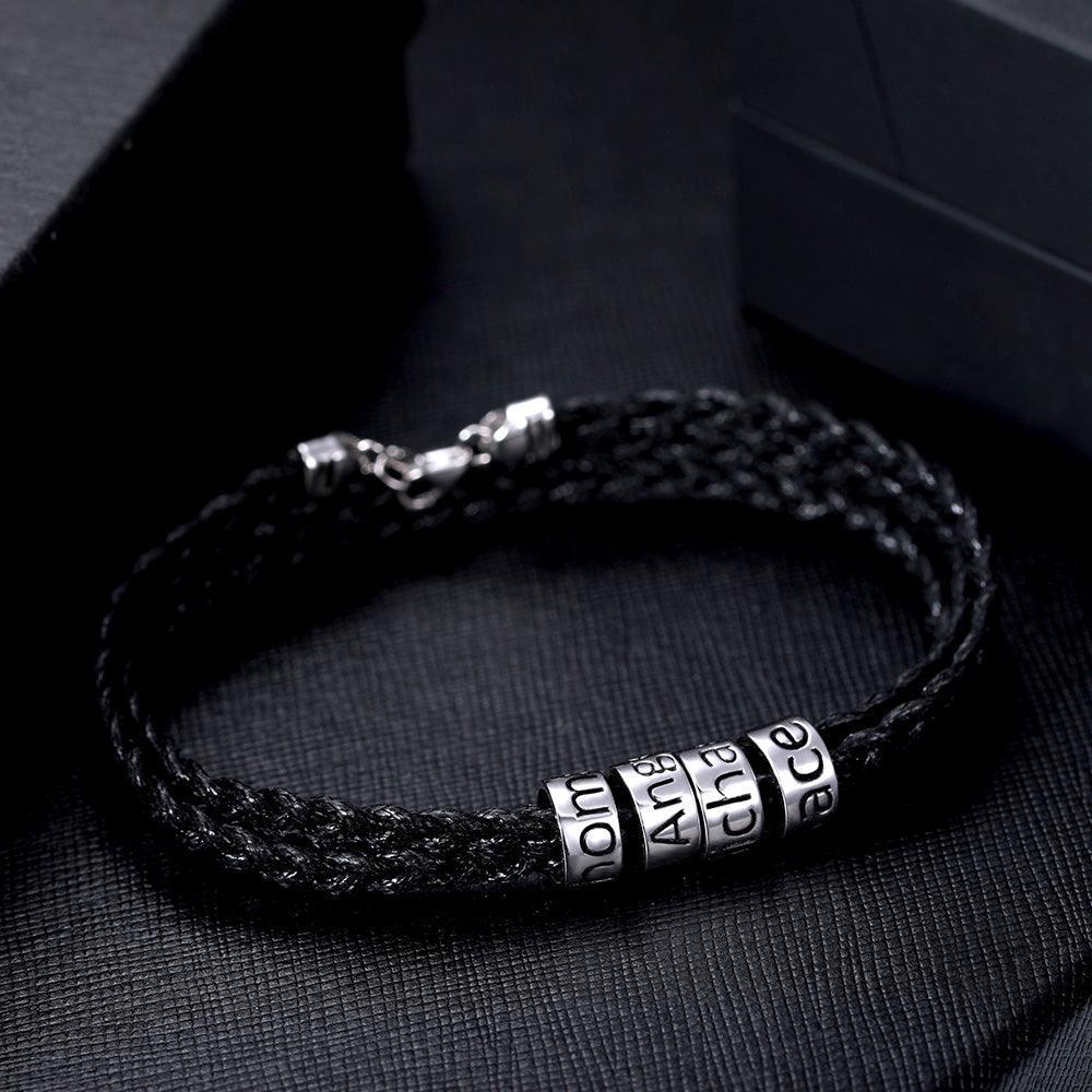Black braided bracelet featuring silver beads engraved with "Mom," "Ang," and "Grace" on a dark background.