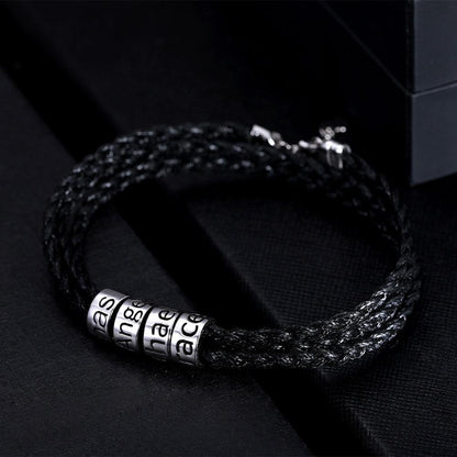 Black braided bracelet with silver beads engraved with "Bas," "Grace," and "Mac" on a sleek background.
