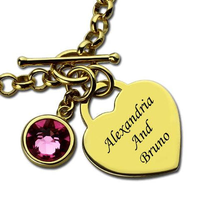 Close-up of a gold-plated personalized heart charm bracelet with a pink birthstone and engraved names "Alexandria and Bruno," featuring a secure toggle clasp.