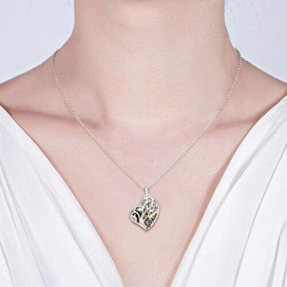 A person wearing a delicate silver necklace with a heart-shaped pendant featuring an intricate tree design and colorful gemstones.