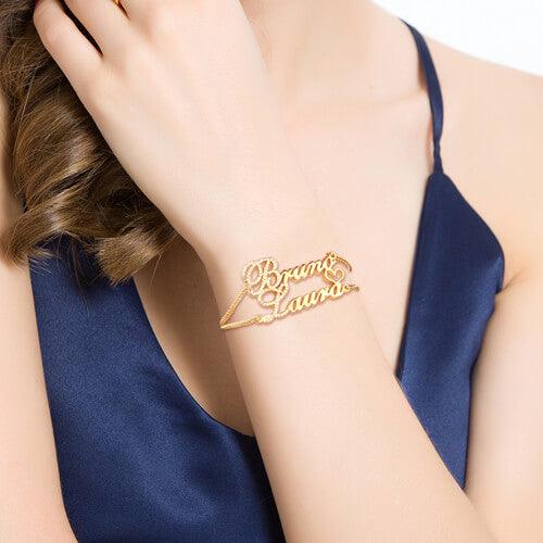 A woman wearing a navy blue dress displays a gold bracelet on her wrist with the names "Bruno" and "Laura" intricately designed in cursive script.