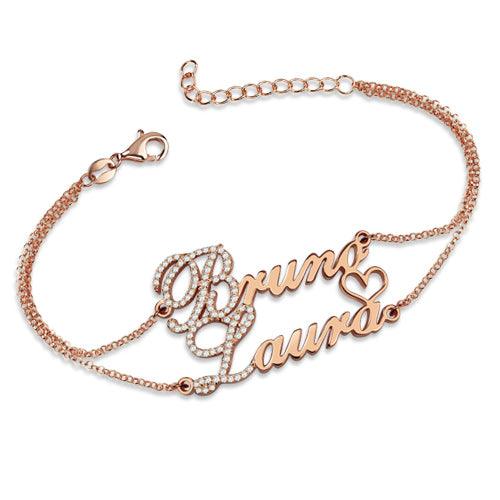 A rose gold bracelet with the names "Bruno" and "Laura" in cursive, featuring birthstones just before the letters B and L, connected by a delicate chain with small diamonds and a heart.