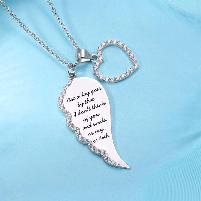 Silver necklace with a wing-shaped charm and a heart, both adorned with rhinestones, against a blue background.