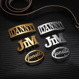 Assorted gold and silver belt buckles with names 'DANNY,' 'JIM,' and 'Janette' on a black textured background with a brown belt.