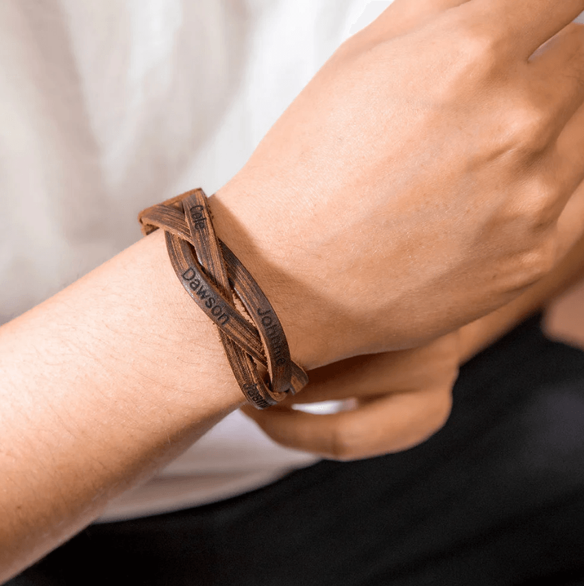 Person wearing a brown leather bracelet engraved with the name Dawson, Cele, John.