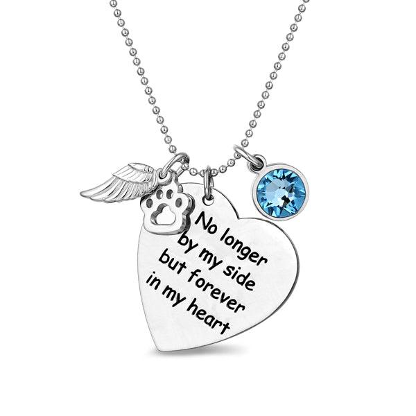 A silver necklace with a heart-shaped pendant engraved with the words "No longer by my side but forever in my heart," alongside a paw print charm, an angel wing, and a blue gem.