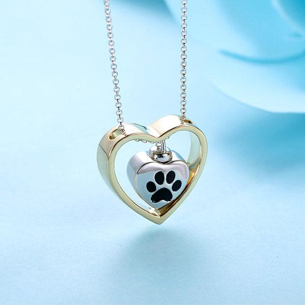 Gold heart-shaped frame with a smaller silver heart pendant featuring a black paw print, on a silver chain.