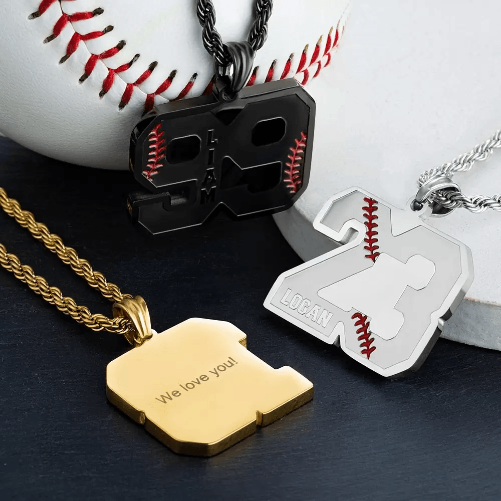 Three baseball-themed number pendants: black "99" for Liam, silver "23" for Logan, and gold with "We love you!" engraved on the back, placed near a baseball.