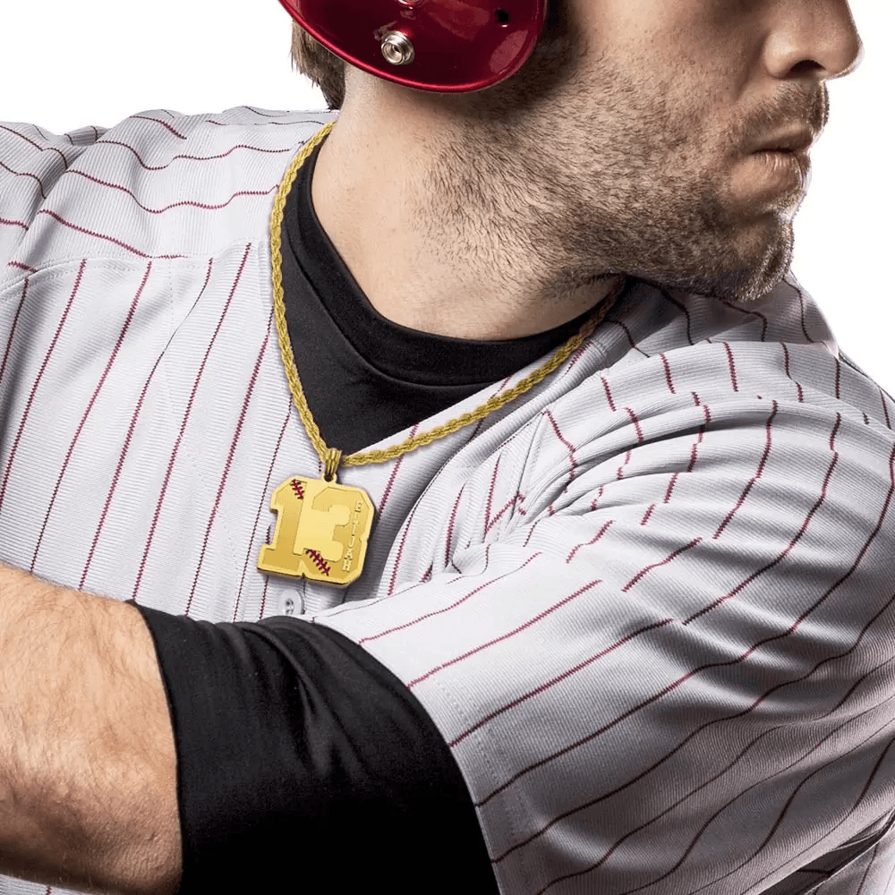 A baseball player wearing a striped jersey and helmet, holding a bat, with a gold number pendant featuring "13" and "Elijah" engraved, hanging on a gold chain.