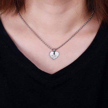 A woman wearing a silver heart pendant engraved with "Daddy's Girl" on a chain, set against a black top.