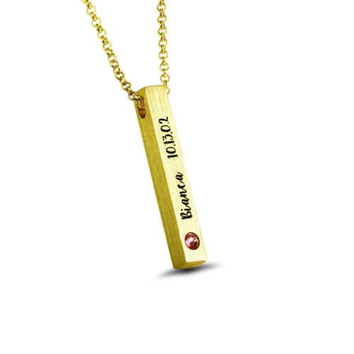 A gold necklace with a vertical bar pendant engraved with "Bianca 10.13.02" and a red gemstone at the bottom left corner, displayed on a white background.