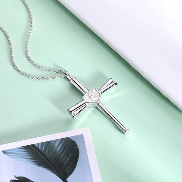 Silver baseball bat cross pendant with embossed number 2, displayed on a light green surface next to a white sheet and leaf print.