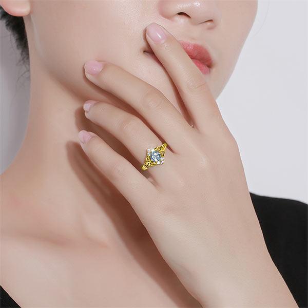 Elegant gold Celtic knot ring with a prominent blue gem on a woman’s finger.