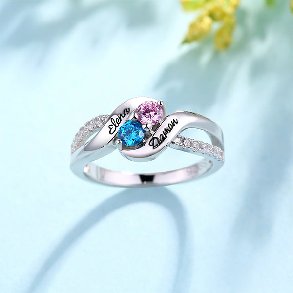 Silver ring with 'Elena' and 'Darren' engraving, pink and blue stones, on a floral background.