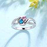 Silver ring with 'Elena' and 'Darren' engraving, pink and blue stones, on a floral background.