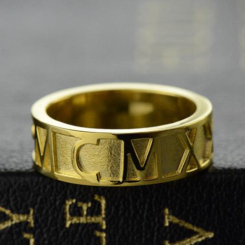 Gold ring with engraved Roman numerals on the outer band, displayed against a textured black background.