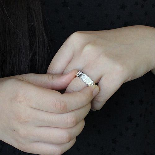 A person wearing a silver ring with engraved geometric patterns, against a dark background with a subtle star design.