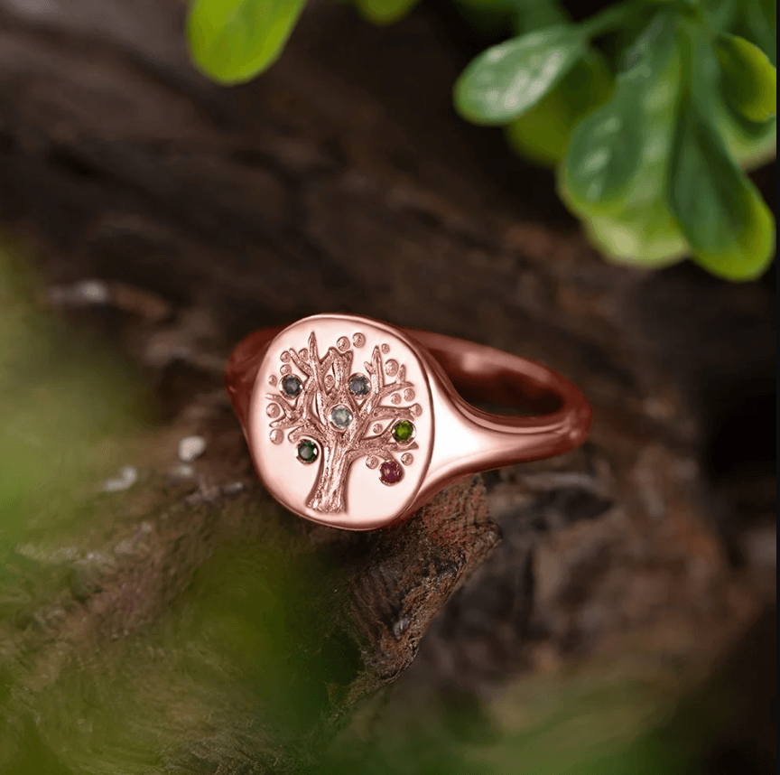 Rose gold family tree ring with embedded birthstones, on a natural wooden backdrop.