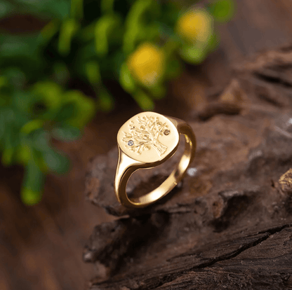 Gold signet ring with a family tree and gemstones on a rustic wooden surface.