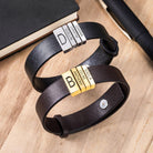 Two curved leather bracelets with engraved beads, one in silver and one in gold, displayed on a wooden table.