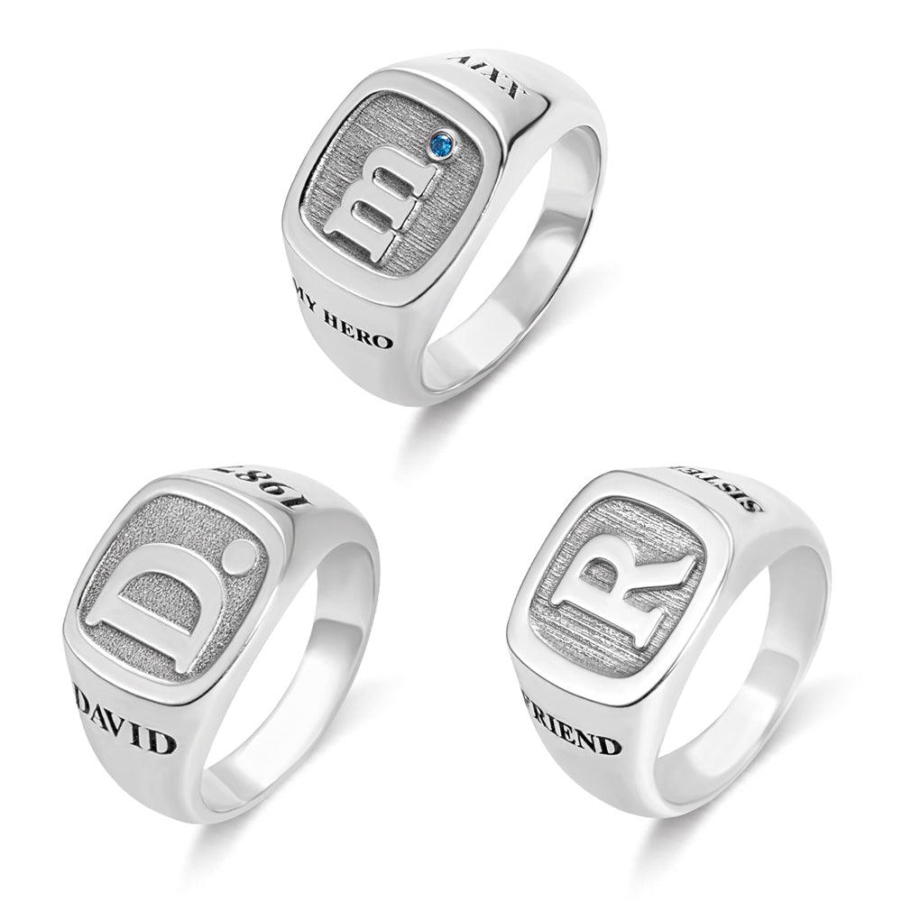 Three silver rings with bold engraved initials: "M" with a blue gem, "D" with the name "DAVID," and "R" with the word "FRIEND," each featuring detailed textures.