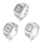 Three silver rings with bold engraved initials: "M" with a blue gem, "D" with the name "DAVID," and "R" with the word "FRIEND," each featuring detailed textures.