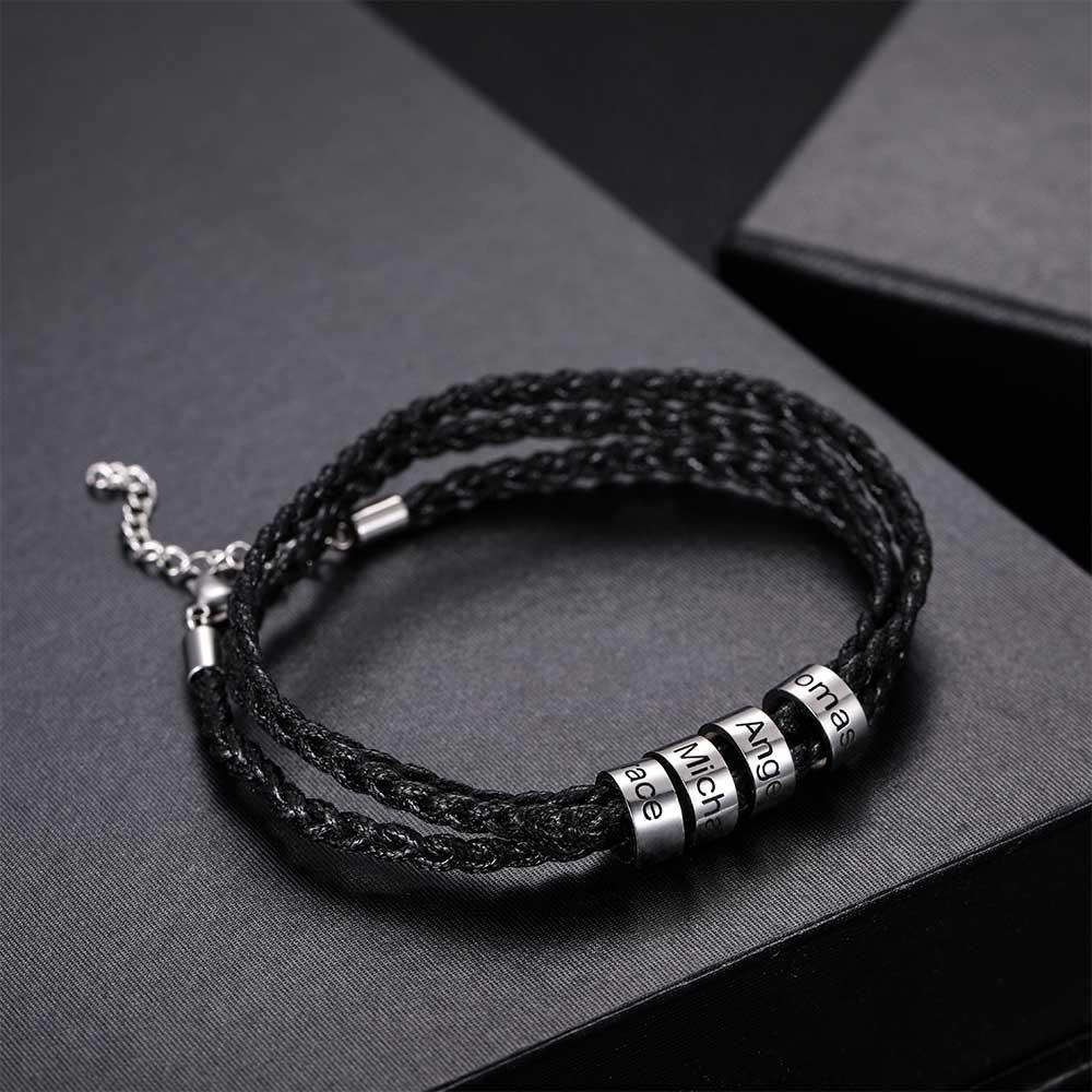 Black braided bracelet with silver beads engraved 'Thomas', 'Angel', 'Michael', 'Grace' on a dark presentation box.