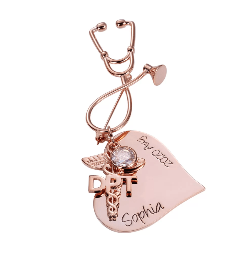 A rose gold nursing brooch shaped like a stethoscope, featuring a medical emblem and personalized text reading "Sophia" and "2020 Aug."