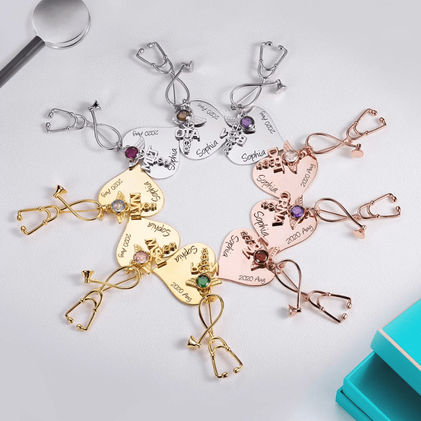 A collection of nursing brooches in silver, gold, and rose gold, each shaped like a stethoscope, featuring a medical emblem, gemstones, and personalized text reading "Sophia" and "2020 Aug."