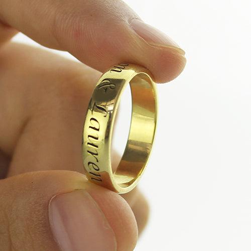 A hand holding a gold ring engraved with names "Lauren" and another partially visible name. The ring has a shiny and smooth surface.