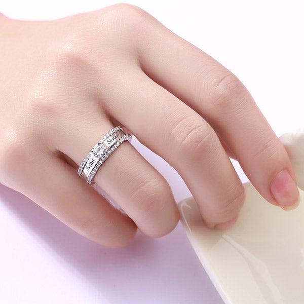 Close-up of a hand wearing a sterling silver double band ring engraved with 'Justin & Sienna' and adorned with cubic zirconia.