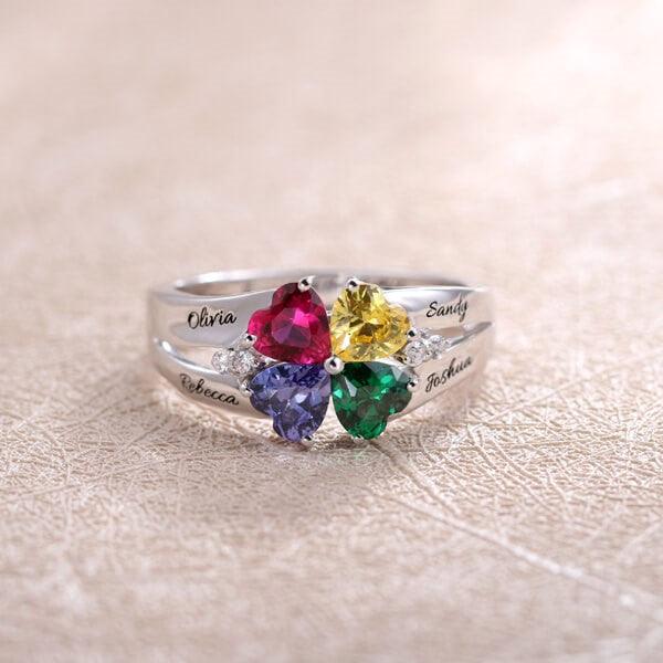 A silver ring with four heart-shaped gemstones in red, yellow, purple, and green, personalized with the names Olivia, Sandy, Rebecca, and Joshua.